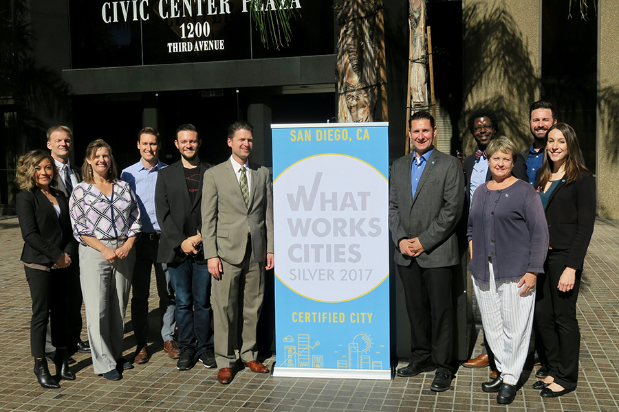 City of San Diego officials pose in front of their What Works City Certification plaque