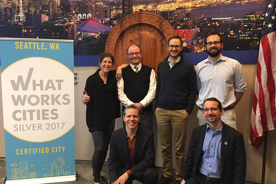 City of Seattle officials pose in front of their What Works City Certification plaque